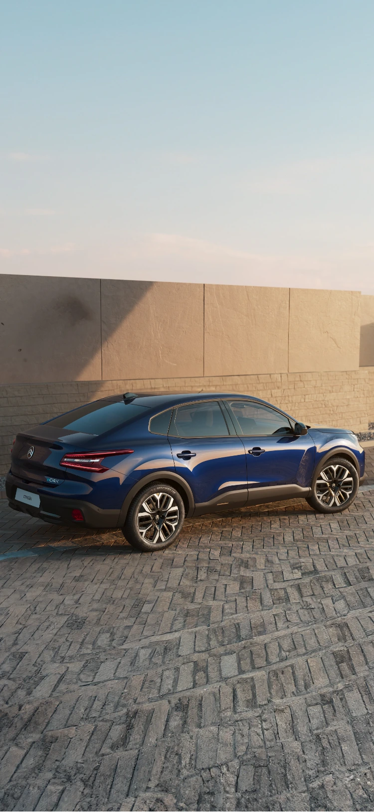 Seitenansicht des Citroën C4 X fährt bei Sonnenuntergang entlang der Küste und zeigt sein elegantes Profil
