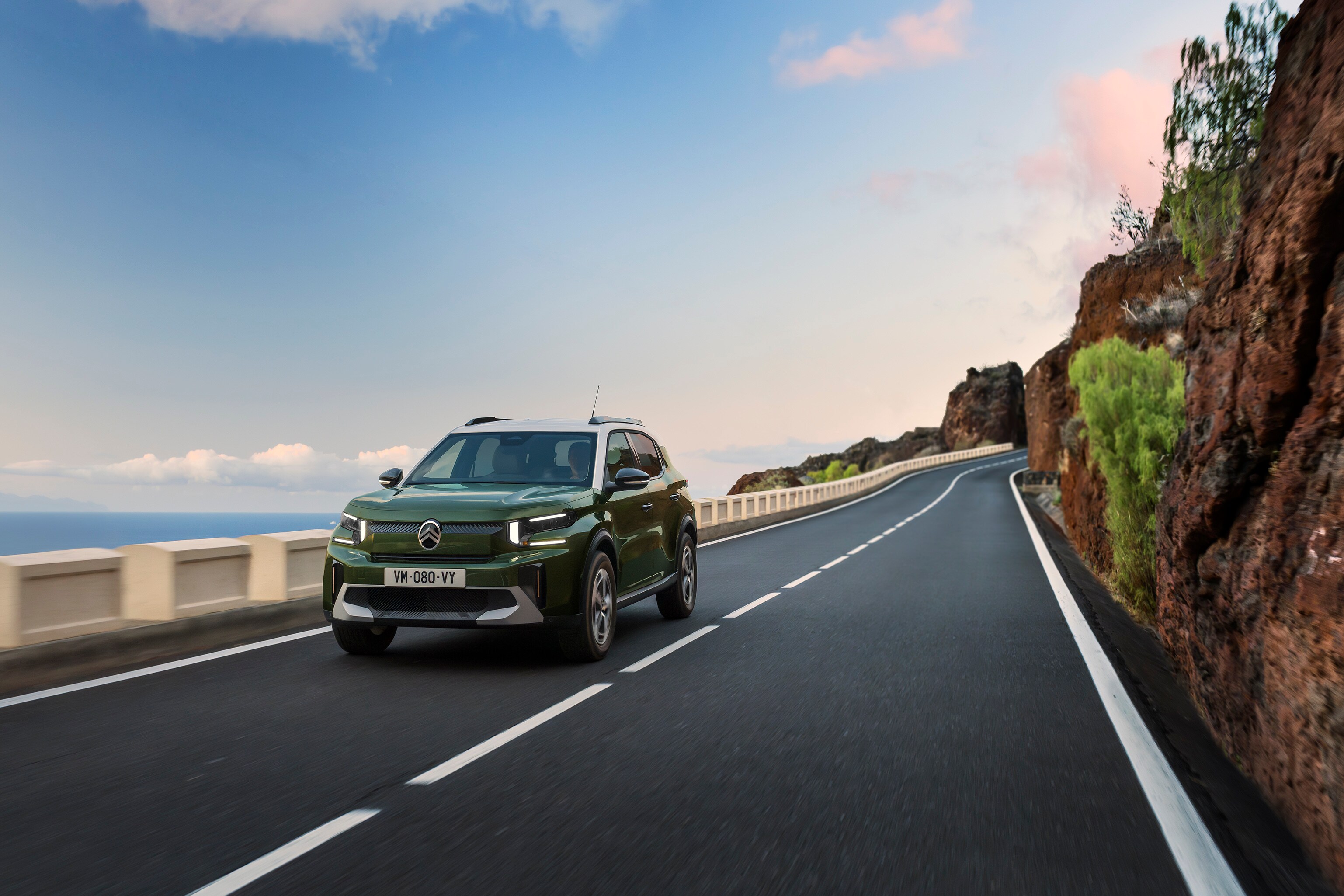 Dreiviertel-Frontansicht während der Fahrt des Citroën ë-C3 Kompakt-SUV auf einer malerischen Straße zeigt agile, sichere und erschwingliche Alltagsmobilität.